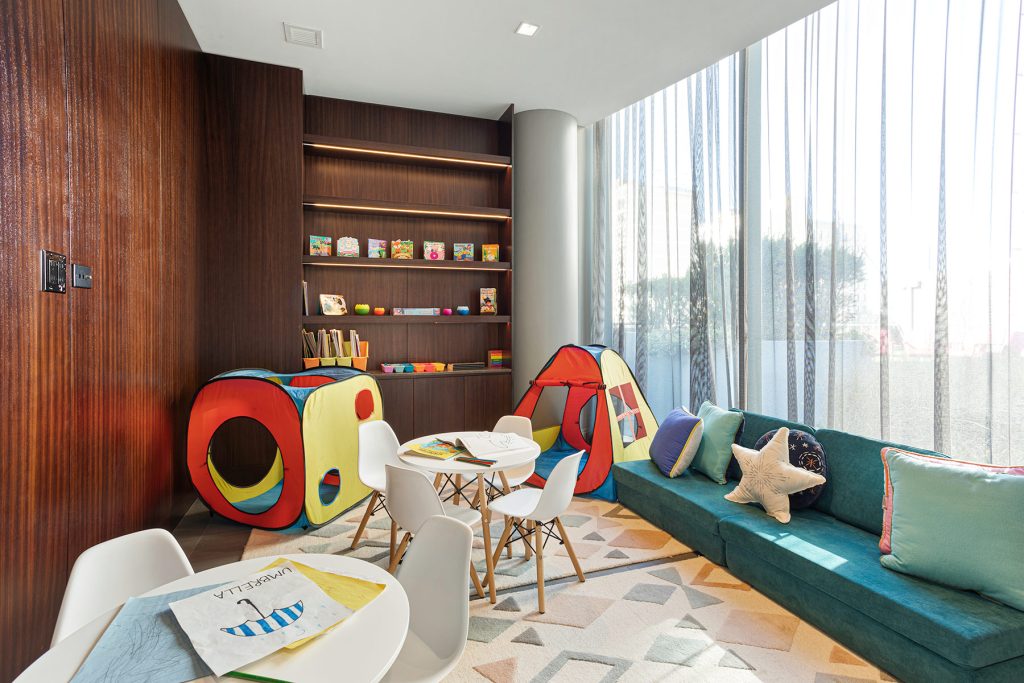 Kids playroom with rocking horse, teal couch, inlay wooden shelfs with toys and table.