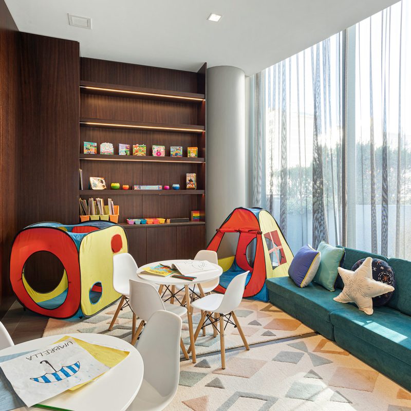 Kids playroom with rocking horse, teal couch, inlay wooden shelfs with toys and table.