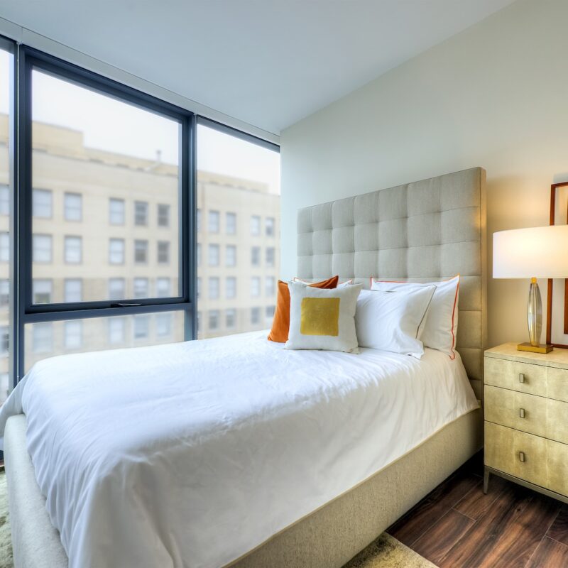 Bedroom with cream colored bed, yellow night stand and views of the city