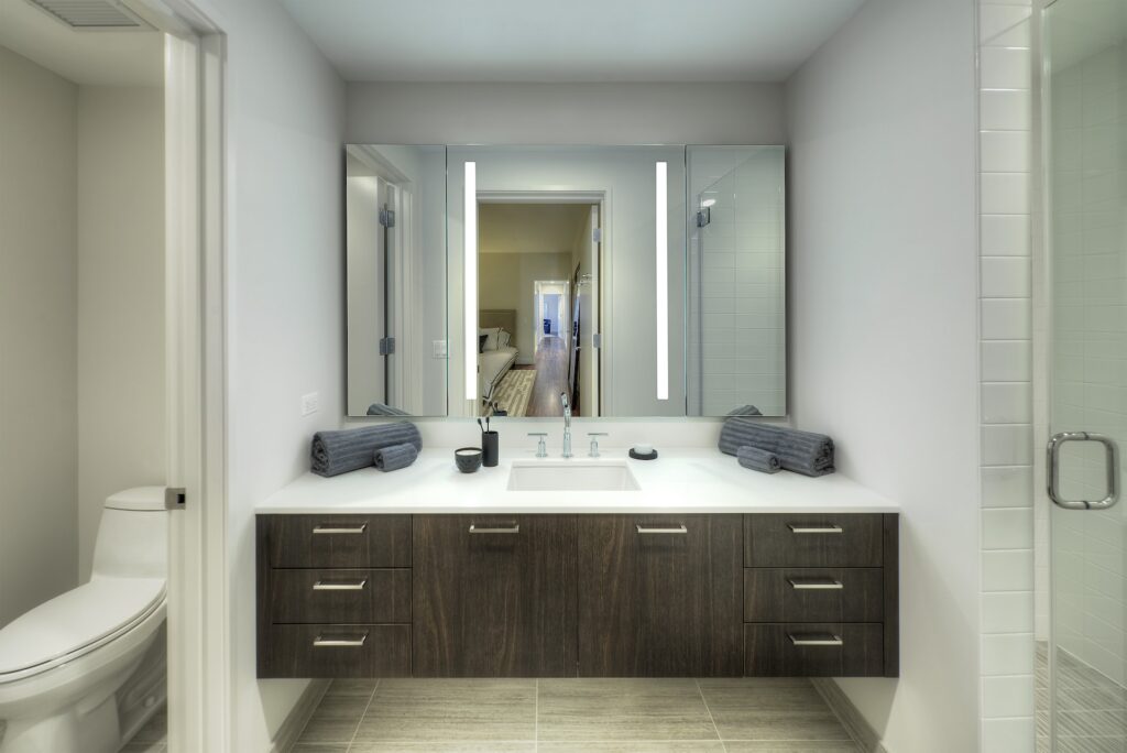View of master bathroom wood vanity with white marble top and large mirror