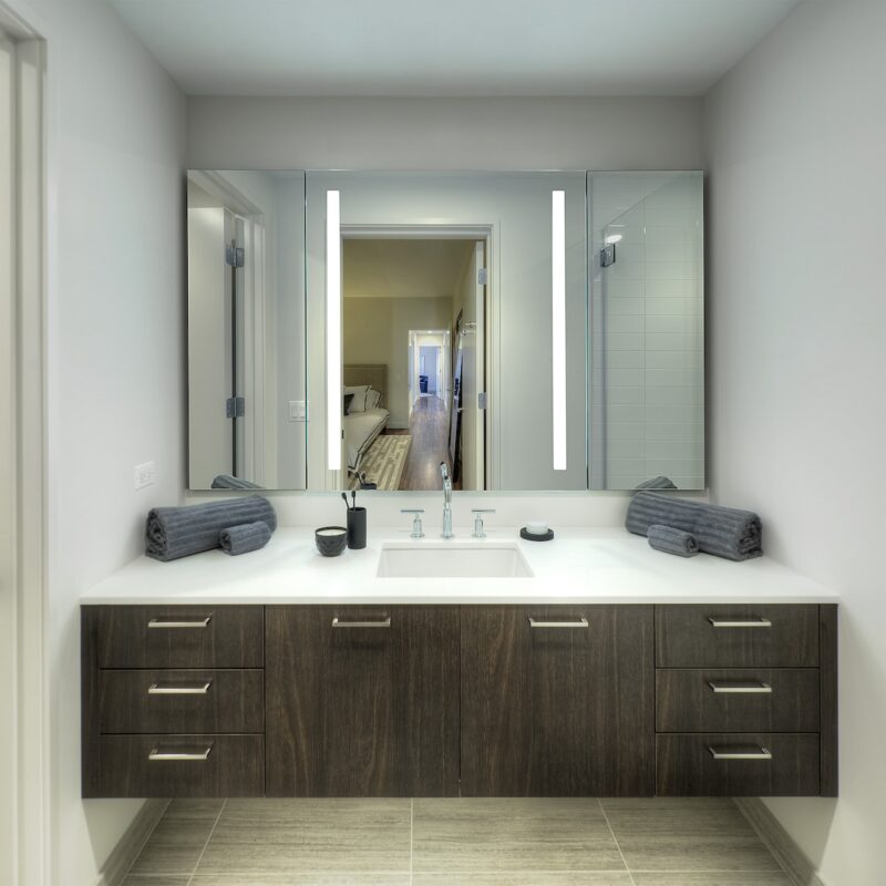View of master bathroom wood vanity with white marble top and large mirror