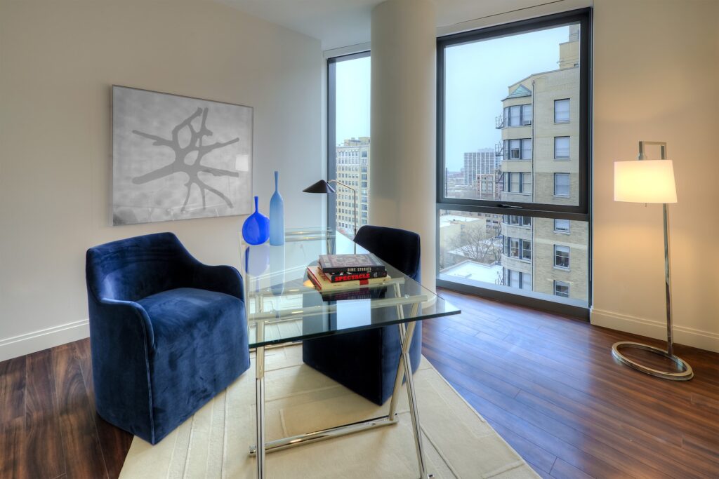 Home office with glass desk, blue cushion chairs and a view of the city